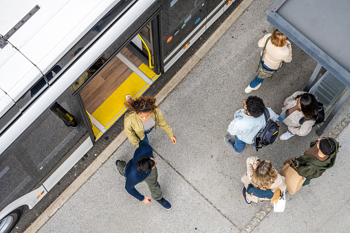 Overhead view of passengers exiting and standing at bus stop in city.
