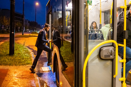 Businessman boarding in bus at bus stop in city.