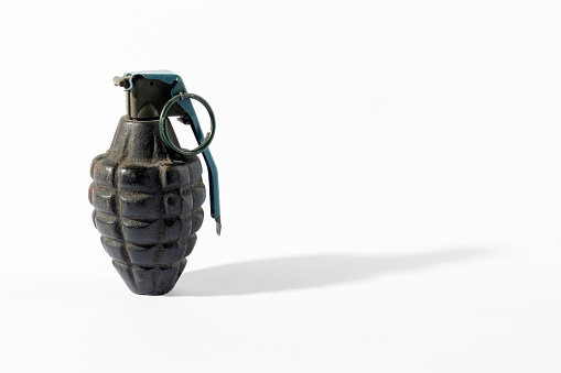 Aged hand grenade with shell covered with dust casting shadow on white background