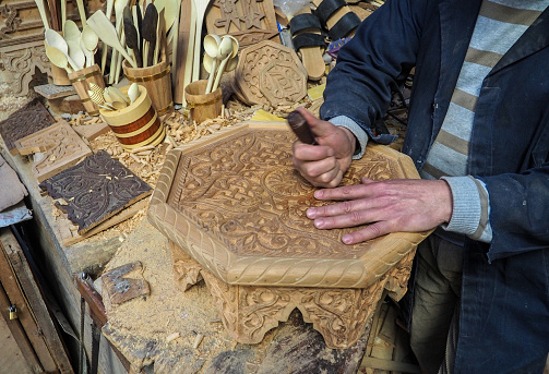 Fez, Morocco - January 07, 2020: Unknown man in his wood working or carving workshop near street market. many wooden souvenirs and products around him, detail to hands