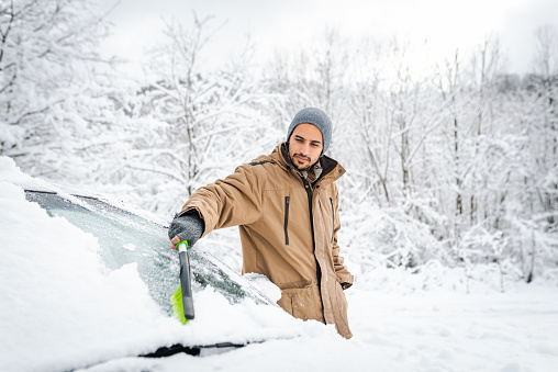 Young man cleaning his car from the snow in a winter day.