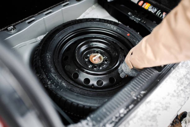 Driver changing spare tyre after accident. Broken and flat car wheel after crash.