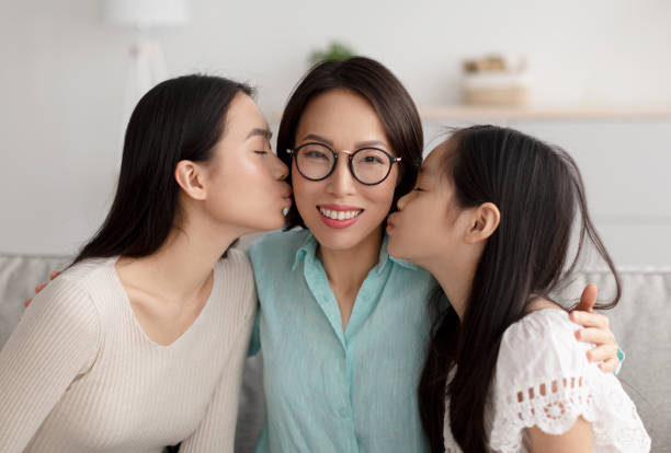 自宅で彼女の大人の娘と小さな孫娘にキスされている眼鏡で陽気な成熟したアジアの女性 - grandmother granddaughter senior adult teenager ストックフォトと画像