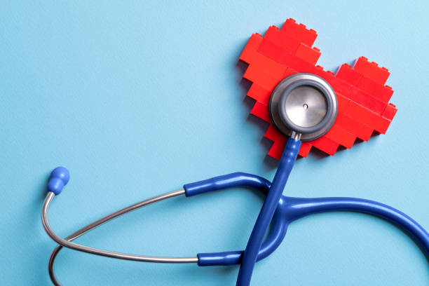Blue stethoscope standing on red heart on blue background stock photo