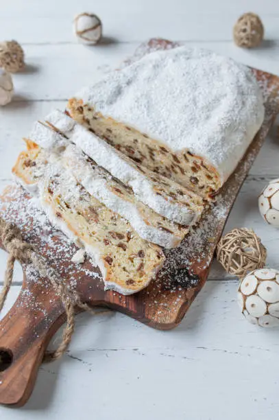 Traditional german christmas stollen or christstollen from Dresden. coated with powdered sugar and baked with raisins, candied fruits, nus and almonds. Served whole and sliced on white wooden background with decoration.