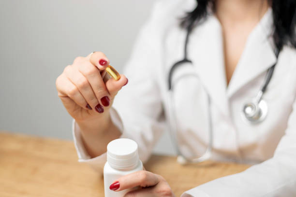 female doctor or pharmacist in white coat holding yellow capsule of omega 3, health care and prevention concept - fish oil cod liver oil doctor holding imagens e fotografias de stock