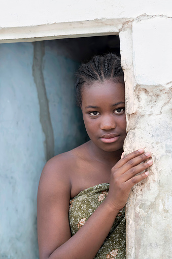 Young Afro girl standing at the door of her house, sad expression, 12 years old, photo