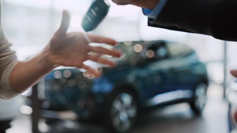 SLO MO Car salesman shake hands and hands over the keys to a new car to a female customer