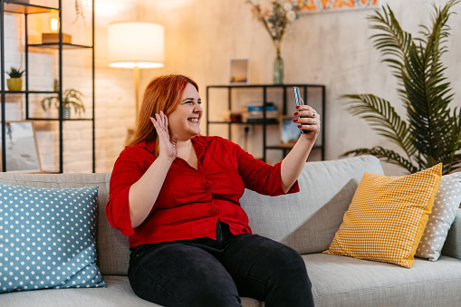 Beautiful young plus size woman having a video call on the sofa at home.