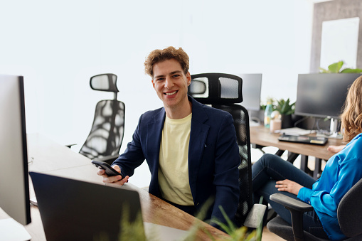 Portrait of a beautiful smiling businessman using his black smartphone in the modern office