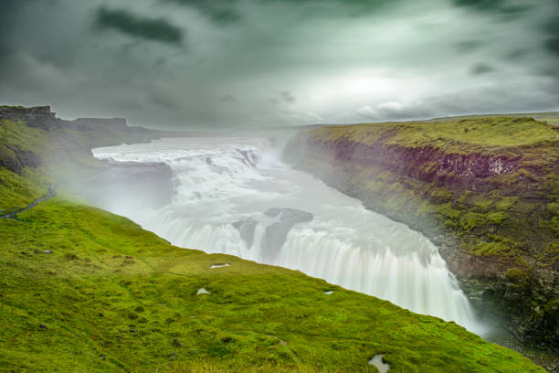 The Gullfoss waterfall in Iceland seen from above on a cloudy stormy day. Tourists are looking at the waterfall on the left. Gullfoss is one of the most popular tourist attractions in Iceland and is part of the Golden Circle tour.