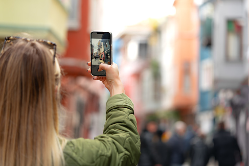 Woman tourist taking photo with phone in the street back view