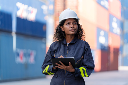 African American dock manager in uniform and safety helmet working and inspector at container cargo with digital tablet. Logistics import and export shipping yard. Transportation and global business concept