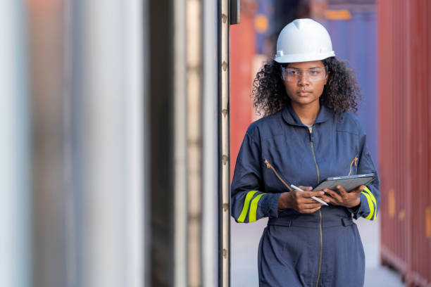 istock African American dock manager in uniform and safety helmet working and inspector at container cargo take some note on clipboard. Logistics import and export shipping yard. Transportation and global business concept 1468536011