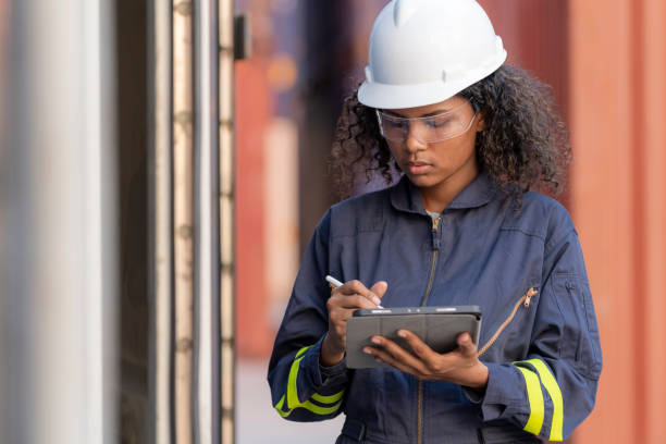 istock African American dock manager engineer in uniform with safety helmet standing at container cargo with digital tablet. Logistics import and export shipping yard. Transportation and global business concept 1468536023