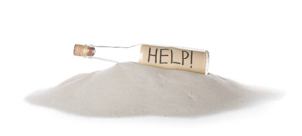 istock Corked glass bottle with Help note on sand against white background 1468539839