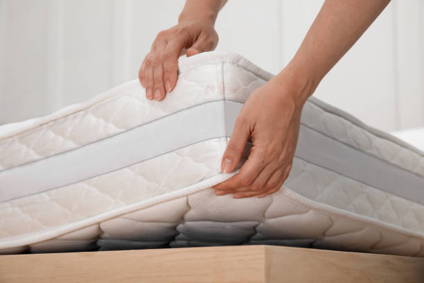 Woman putting soft white mattress on bed indoors, closeup stock photo