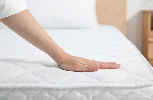 Mujer tocando un suave colchón blanco en la cama en el interior, primer plano photo