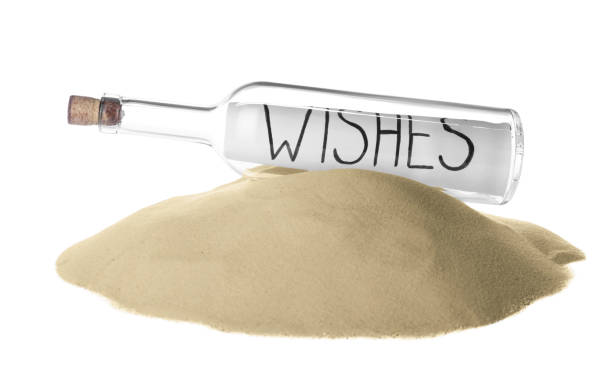 Corked glass bottle with Wishes note on sand against white background Corked glass bottle with Wishes note on sand against white background castaway stock pictures, royalty-free photos & images