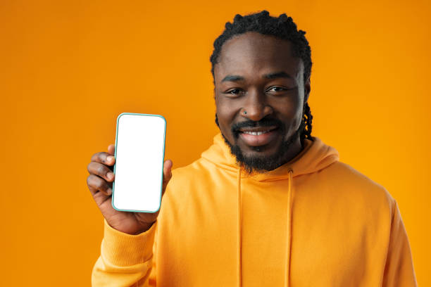 istock Smiling african man pointing at cellphone with blank screen with copy space 1468542401