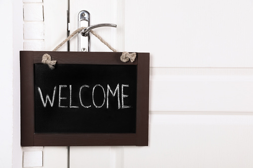 Small chalkboard with word Welcome hanging on door handle, space for text
