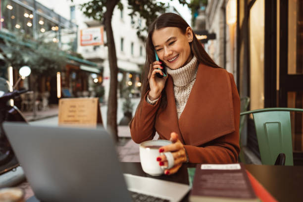 istock Smiling young woman using laptop and and talking on the phone while sitting in cafe 1468543227