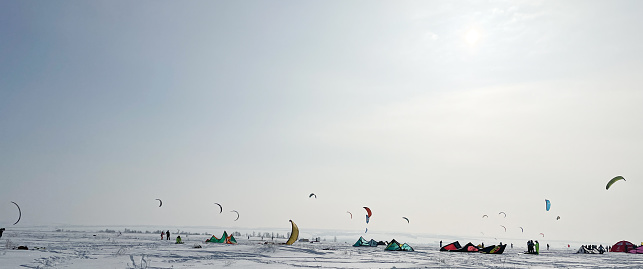 A lot of people are engaged in snowkiting in a snowy area, surrounded by tents