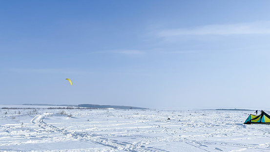 A person is engaged in snowkiting in a snowy area, next to a tent. Parachuting.