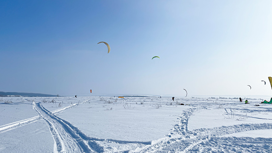 A lot of people are engaged in snowkiting in a snowy area, surrounded by tents