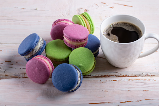 Lots of colored macaroons and a white cup of coffee on a white wooden table