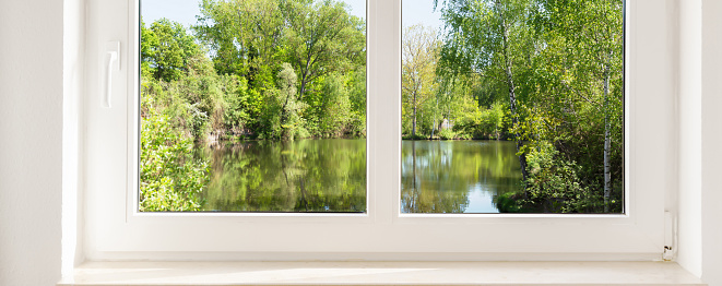 window view into the idyllic green nature with a pond, background with copy space for product presentation on the white window sill, concept for rental, travel, vacation, real estate business