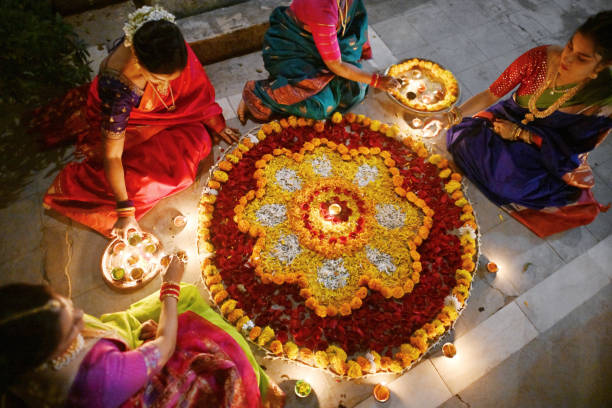 High angle view of beautiful Indian women in saris (Indian traditional wear) decorating Rangoli with oil Lamps (Diya) High angle view of a beautiful Indian women dressed in a traditional festive wear decorating Rangoli with oil Lamps (Diya) sitting near a temple of a Palace in Rajasthan flower rangoli stock pictures, royalty-free photos & images