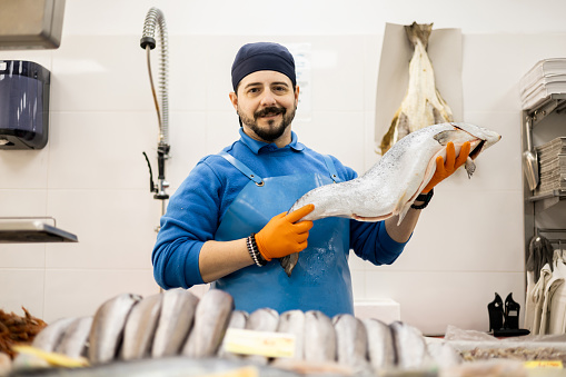 A uniformed middle-aged fishmonger is showing salmon to the camera, selling food, a concept of small and medium enterprises.