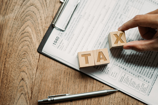 Wooden cubes with the word tax with US Income Tax Return forms 1040 to complete your tax legal, financial payment Profit and investment taxation to the government on behalf of a company or individual.