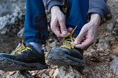 Close up of young man hiker tying shoelaces and getting ready for trekking in mountain