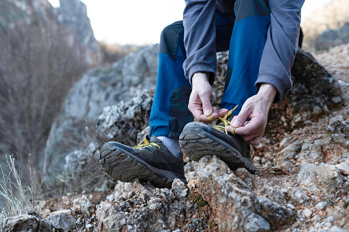 Close up of young man hiker tying shoelaces and getting ready for trekking in mountain