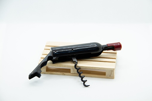 Wine bottle shaped corkscrew laying atop a wooden stand isolated on white background