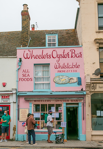 Customers outside Wheelers Oyster Bar on Whitstable High Street in Kent, England, with illustrations and contact numbers visible. This is the oldest restaurant in Whistable having been founded in 1856.