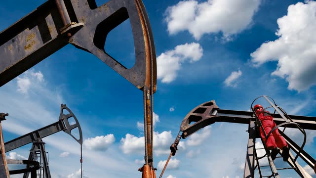 Oil Worker and Three Oil Well Pump Jacks Against Blue Sky with Clouds