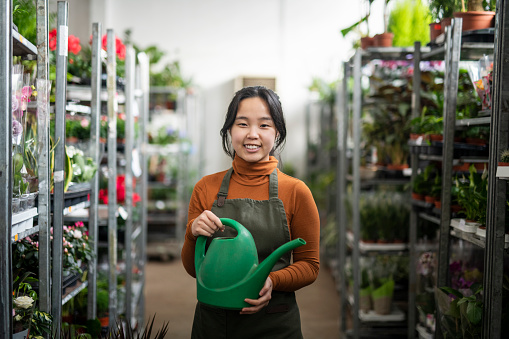 Portrait of young asian woman holding a watering can in a flower shop.