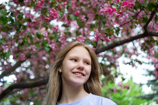 Smiling teenage girl in sakura flowers in spring. Hanami celebration in sakura blooming garden. . High quality photo