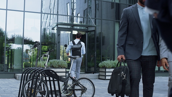 Corporate people walking enter office building. Shared parking at downtown area. Rental eco-friendly vehicles electric scooter bicycle standing at business center. Alternative city transport concept.