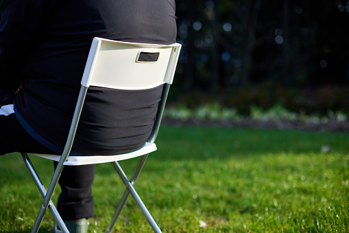 Closeup man sitting on white folding chair on grass