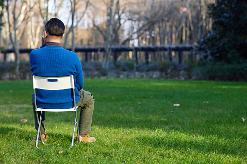 A man sits on a white folding chair on the lawn
