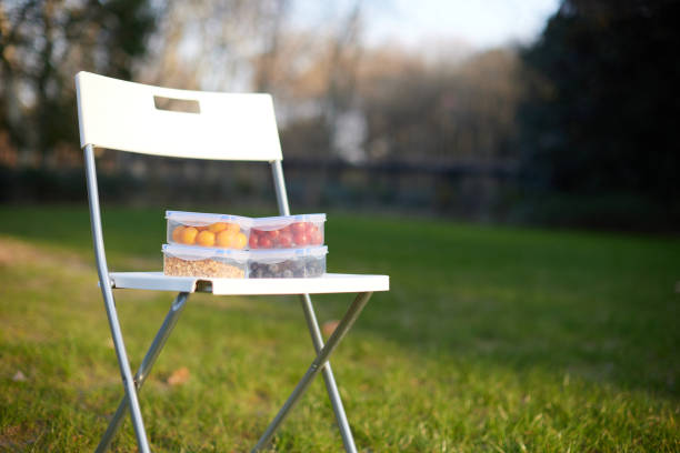 Four Tupperware filled with tomatoes, oranges and granola on a white folding chair on super low