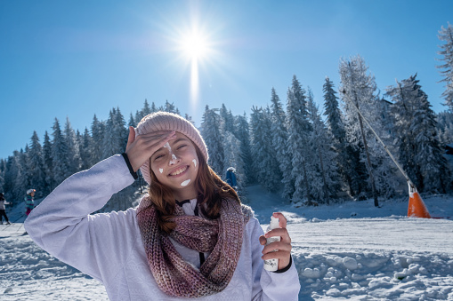 A teenage girl applies sunscreen while skiing because the sun is hot.