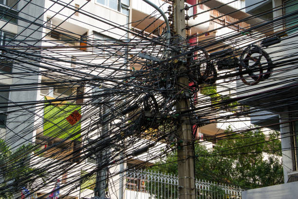 caos de cables y alambres en bangkok, tailandia, cables eléctricos y telefónicos enrollados en un poste de luz - uncoordinated fotografías e imágenes de stock