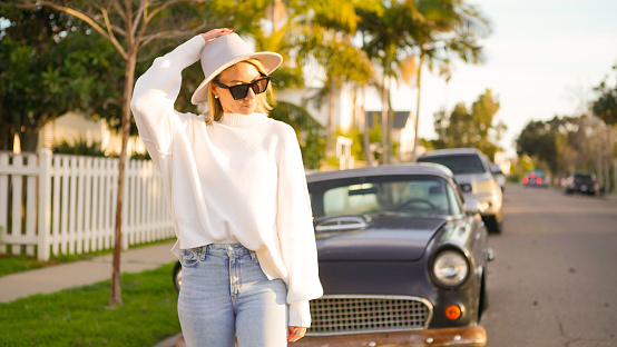 Happy woman in red dress enjoy sunset near country road and classic Vintage sports car. Romantic freedom travel concept. Road trip