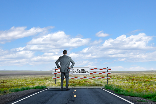 A businessman stands at the end of a road and looks past the construction road block that has a 