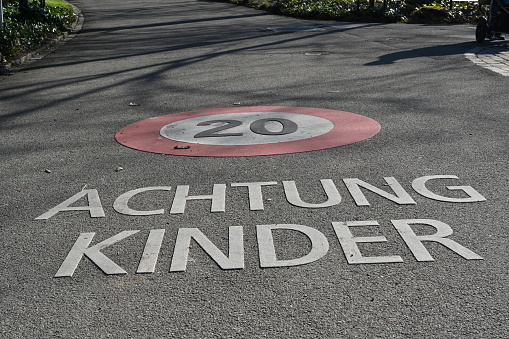 Street with sign for speed limit 20 kilometer per hour and inscription in German language saying attention children. The speed limit and the inscription are marked on the ground.